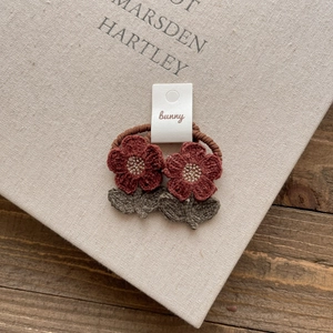 Close-up of handmade crochet flower hair ties with burgundy petals and green leaves