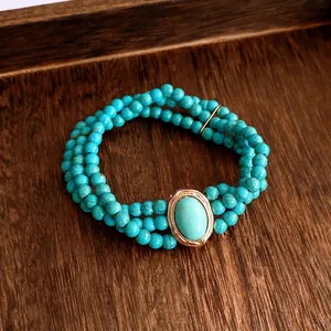 Bracelet à trois rangs de perles turquoise et monture dorée sur fond de bois sombre