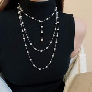 Détail montrant le collier de perles élégant à trois rangs avec pendentif goutte sur un pull