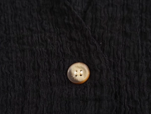 Close-up of black textured fabric and marble-patterned amber button on a sleeveless top