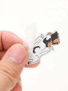 Detail showing hand peeling protective film off the Goofy character acrylic keychain