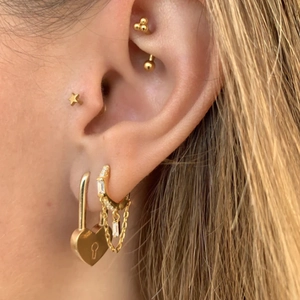 Detailed close-up of stacked gold earrings featuring heart lock and star studs