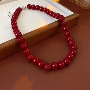 Close-up of a red round bead necklace with a silver clasp on a wooden tray