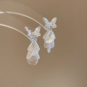 Détail de boucles d'oreilles papillon en argent avec pompons en nacre blanche superposés