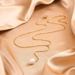 Detailed shot of golden Y-shaped necklace with pearl pendant on champagne silk fabric