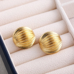 Close-up of golden textured spherical stud earrings displayed in a beige jewelry box