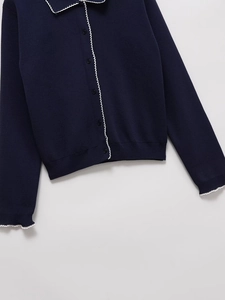 Detail of dark blue knit cardigan showing scalloped white trim and single-breasted buttons