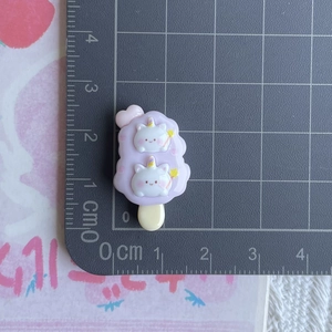Detailed view of a purple resin popsicle charm with cartoon cats on a cm scale mat