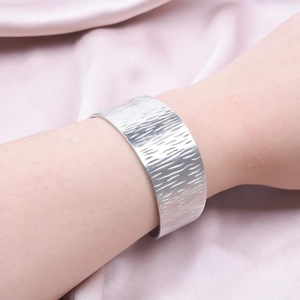 Detail of silver brushed stainless steel cuff bracelet on a soft silk background