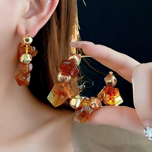 Detailed view of amber resin and gold geometric beads on hoop earrings worn by a model