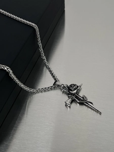 Close-up of silver thorn rose cross necklace on a brushed metal background with gift box