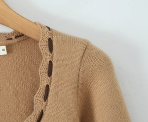 Dettaglio del collo della maglia kaki con trama del tessuto su una gruccia in legno