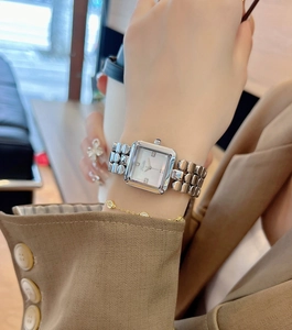 Close-up of a silver square watch with shell dial on a woman's wrist with metal strap