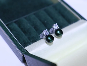Macro view of dark green pearl earrings with cubic zirconia in a velvet box