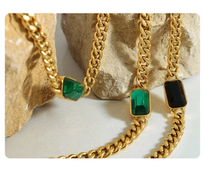 Detail of gold Cuban chain necklace with green and black rectangular gemstones on a stone