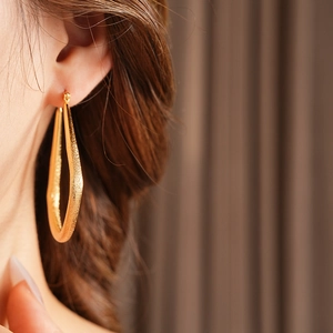 Gros plan sur une boucle d'oreille dorée en forme d'éventail avec finition texturée