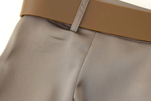 Detail of high-quality brown satin wide-leg pants with a matching smooth leather belt
