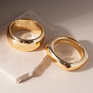Polished gold geometric round and square chunky acrylic bangles on a stone pedestal
