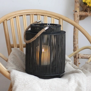 Nordic handwoven black lantern with jute handle and warm LED candle on a rattan chair