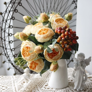 Detail of silk peony bouquet with orange berries in white vase on lace tablecloth