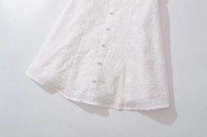 Detail of white dress featuring floral embroidery and decorative cloth-covered buttons