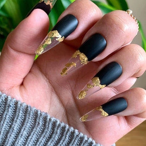 Detailed view of matte black and gold foil long stiletto press-on nails on hands