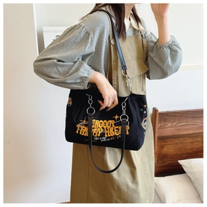 Detail of black canvas tote bag featuring vibrant colorful letter embroidery and chain strap