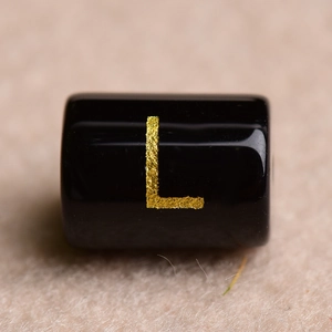 Macro shot of a black cylindrical bead with gold letter L for DIY jewelry making