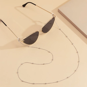 Detailed view of cat-eye sunglasses with a gold beaded metal chain on a beige backdrop