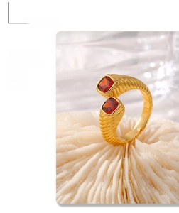 Close-up of golden spiral band ring featuring two square red zircons on white pedestal