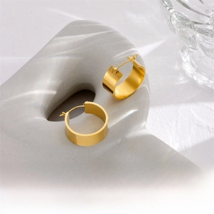 Macro detail of wide gold hoop earrings with polished finish on a ceramic stand
