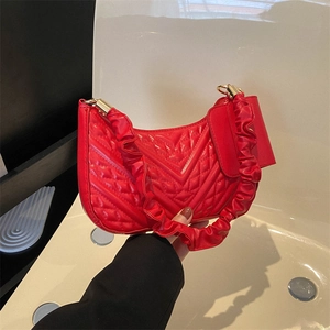Detail of red quilted faux leather handbag with ruffled shoulder strap and gold buckle