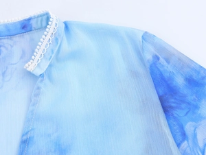 Dettaglio della camicetta in chiffon tie-dye blu con rifiniture in pizzo bianco sullo scollo