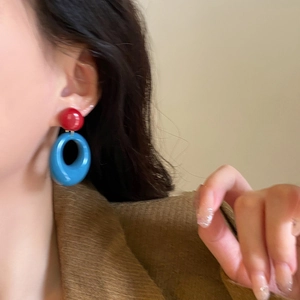 Detail view of retro red and blue resin hoop earrings worn by a model in soft lighting
