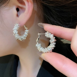 Detailed close-up of irregular silver hoop earrings with shimmering pave-set crystals
