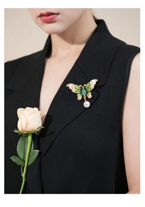 Detail of butterfly brooch with green enamel and pearl drop on a black vest outfit