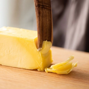 Teak wood spreader knife cutting yellow butter on a wooden board in a warm kitchen