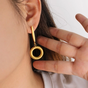 Close-up of a model wearing gold geometric bar and circle drop earrings with relief texture