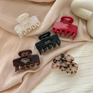Five assorted acetate hair claws in pearl, red, and shell patterns on satin fabric