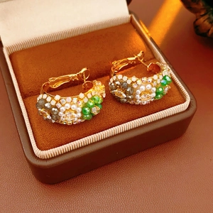 Macro detail of vintage gold C-shape hoop earrings with pearls and colorful gemstones