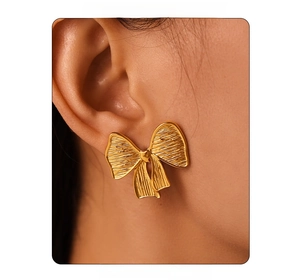 Close-up of golden brushed bow earrings worn by model with textured metal finish