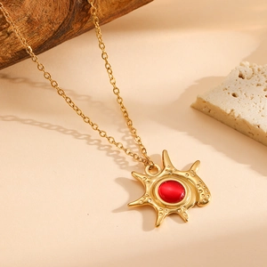 Detail of 18K gold plated sunburst pendant necklace with a central red gemstone inlay