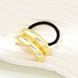 Detail of a gold metallic hair tie on a white tray, showing polished mirror finish and band