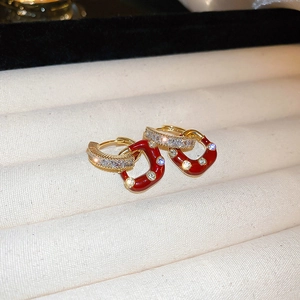 Detail of gold-plated red enamel earrings with white zircon accents on beige velvet