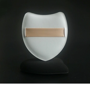 Close-up of a white shield-shaped marshmallow powder puff with beige ribbon on black stand