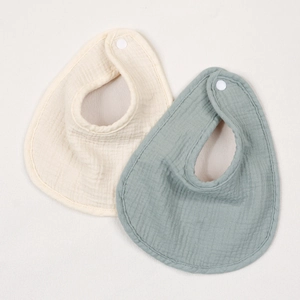 Set of two soft cotton muslin baby bibs in cream and sage green with adjustable snaps
