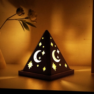Close-up of pyramid-shaped night light with moon and star cutouts casting warm yellow glow