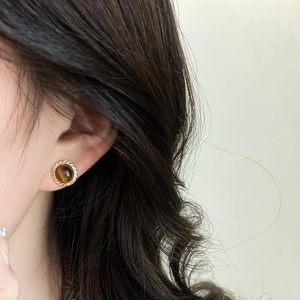 Golden round stud earrings featuring brown cat's eye stone on a female model