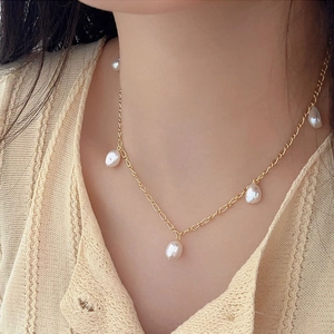 Close-up of elegant gold chain necklace with five irregular baroque pearls on a model