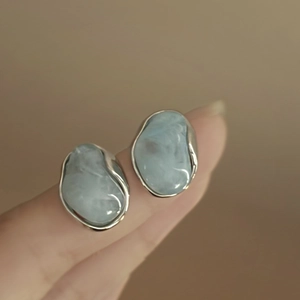 Détail macro de boucles d'oreilles pierre bleue claire serties d'argent sur main